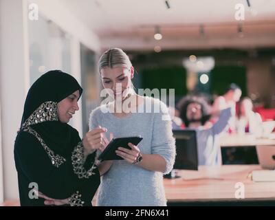 Blonde et moderne femme d'affaires musulmane amis collaborant en équipe et travaillant sur tablette. Une équipe diversifiée dans un bureau à espace ouvert moderne en arrière-plan Banque D'Images