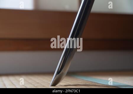 Gros plan d'une épée samouraï poussée dans le tatami mat. Katana est en acier tranchant. Une journée ensoleillée. La fenêtre Shoji est en arrière-plan. Banque D'Images