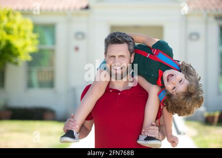 Un père qui donne son pigeyback après son retour de l'école. École, famille, éducation et concept de plein air. Visage amusant pour les enfants. Banque D'Images