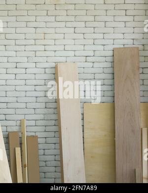 Les planches en bois de différentes tailles s'appuient sur un mur de briques blanches. Ambiance de travail matinale dans la salle d'atelier. Banque D'Images