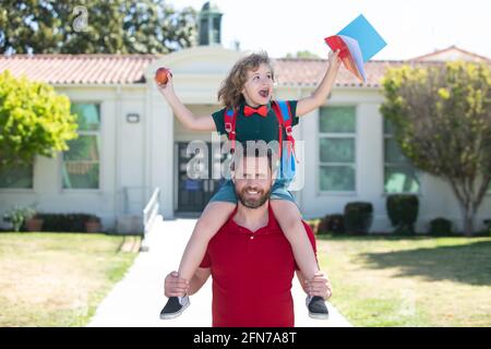 L'homme et l'enfant heureux stupéfié de pigeyback près de l'école. Père marchant fils à l'école. Parent et élève de l'école primaire garçon avec sac à dos. Banque D'Images