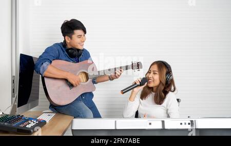 Une jeune femme asiatique chante tout en jouant un clavier électrique devant un mur blanc. Son petit ami joue de la guitare ensemble. Musiciens produisant de la musique en pro Banque D'Images