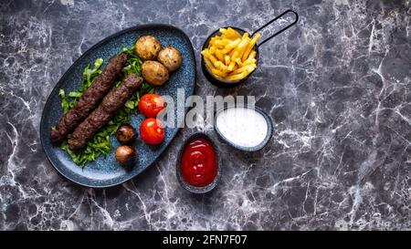 Patties cylindriques Seekh kebab faites avec de la viande hachée assaisonnée grillée sur une brochette. Sur une table marmor blanche noire. Banque D'Images