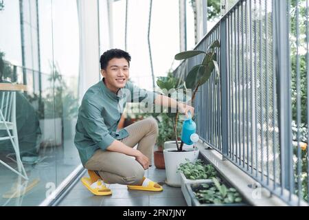 Attrayant jeune homme sur l'appartement balcon arrosoir plantes dans la boîte De la arrosoir bleue Banque D'Images