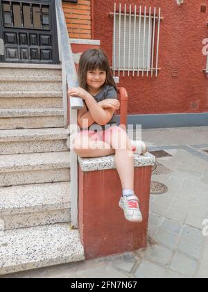 Petite fille souriante assise à côté de la main courante d'un escalier de porte en été Banque D'Images