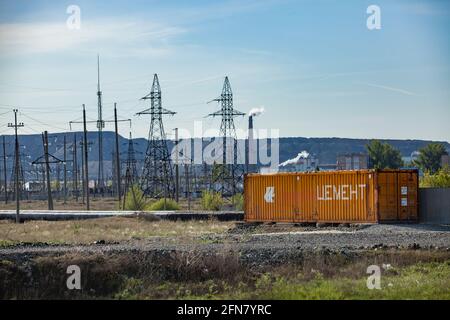 Khromtau, Kazakhstan:vue sur la zone industrielle minière.conteneur brun (titre: Ciment), tours électriques, cheminée avec fumée.décharges de roche, ciel bleu. Banque D'Images