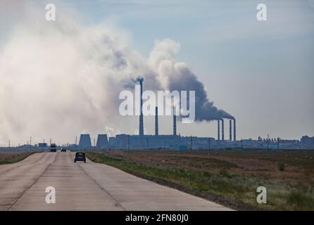 Route en dalles de béton avec voitures et silhouette de centrale électrique à l'horizon. Ciel gris nuageux. Pavlodar, Kazakhstan Banque D'Images