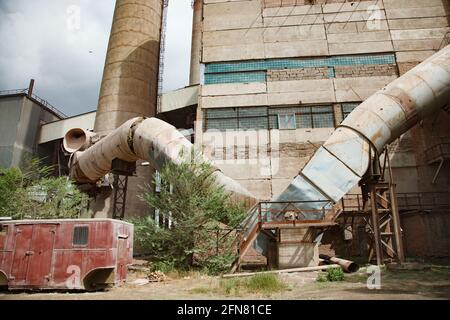 Temirtau, Kazakhstan : usine de ciment soviétique dépassée. Ciment construction industrielle, tubes métalliques. Route sale, ciel bleu. Banque D'Images