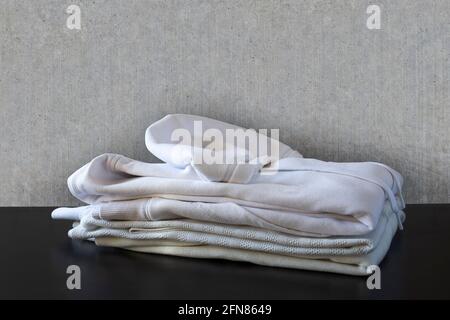 Pile de vêtements blancs devant un mur en béton et sur un sol noir. Chemise, chemise et sweat-shirt Banque D'Images