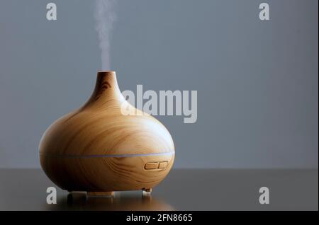 Bouteille d'huile essentielle dotée d'un humidificateur électrique à ultrasons qui émet des gouttelettes d'eau atomisées sur un fond sombre. Le dispositif est de forme ronde avec Banque D'Images