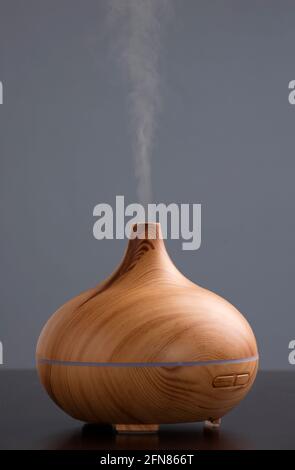 Bouteille d'huile essentielle dotée d'un humidificateur électrique à ultrasons qui émet des gouttelettes d'eau atomisées sur un fond sombre. Le dispositif est de forme ronde avec Banque D'Images