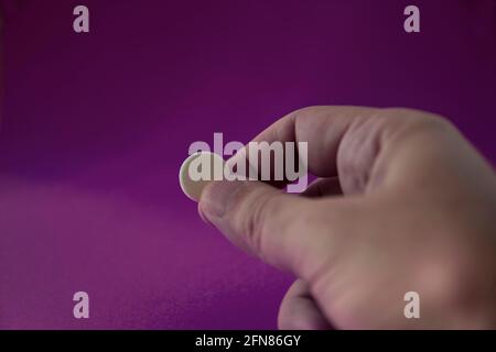Main et doigts tenant la capsule de médicament devant le fond violet. Comprimé sélectif de focus. Banque D'Images