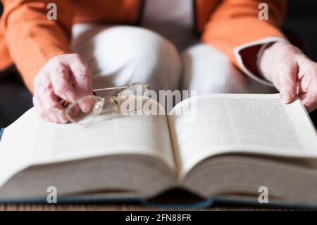 Femme âgée lisant un livre et dans sa main elle tient une paire de lunettes. Banque D'Images