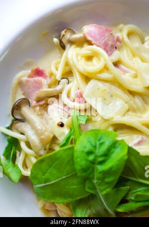 Pâtes sauce carbonara. Recouvrez les spaghetti traditionnels de bacon, de jambon de porc, de parmesan, de champignons et de basilic frais sur une assiette blanche. Bac de cuisine italienne Banque D'Images