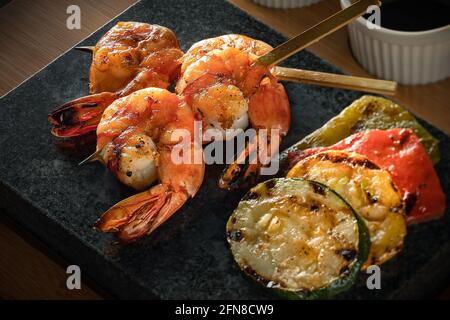 Gros plan sur des brochettes de crevettes servies avec des courgettes grillées, des poivrons rouges et des poivrons verts sur une assiette foncée, une belle sélection de plats de barbecue coréens Banque D'Images