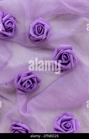 fausses roses pourpres sur le tissu en mousseline de couleur pourpre ou lilas pour les arrière-plans. vue du haut Banque D'Images