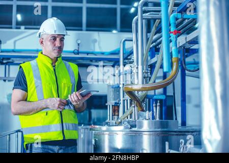 Un technicien travaillant en usine utilisant une tablette pour vérifier la conduite d'eau de la chaudière de maintenance en usine. Banque D'Images
