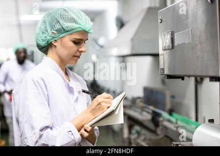 Contrôle de la qualité et sécurité alimentaire le personnel des femmes caucasiennes inspecte la norme de produit dans la chaîne de production de l'usine d'aliments et de boissons. Banque D'Images