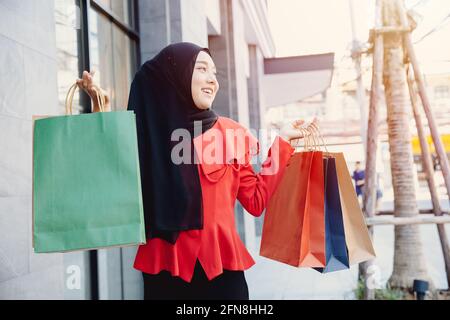 Shopping arabe musulman adulte femme en voile hijab vêtements tenant des sacs marcher dans la rue de la ville appréciez sourire heureux. Banque D'Images