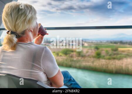 Femme assise autour d'un verre sur un patio extérieur découvrez une balustrade en verre surplombant la rivière et la campagne ci-dessous dans un au-dessus du sh Banque D'Images