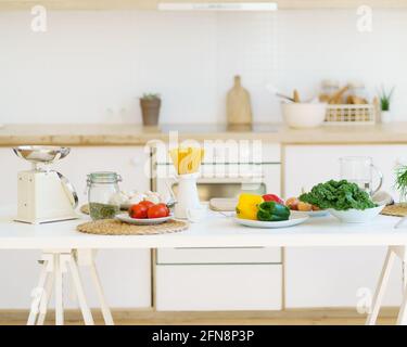 Cuisiner des aliments sains. Pâtes italiennes, légumes frais, graines de citrouille, balances et autres ingrédients sur table en bois blanc sur fond flou de comptoir de cuisine dans l'appartement moderne lumineux Banque D'Images