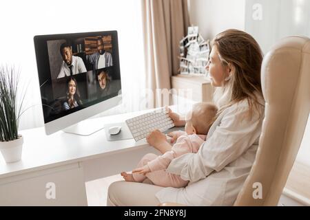 Jeune mère indépendante caucasienne avec bébé travaillant sur un ordinateur portable de la maison. Lieu de travail d'une femme indépendante étudiante avec un enfant tout-petit. Séjour à la maison mère célibataire Banque D'Images