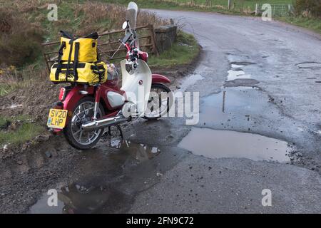 dh Roads SCOTLAND UK Pothole moto par des nids-de-poule profond trou dans la surface endommagée de la route Covid 19 hiver dommages près de la mauvaise route Banque D'Images