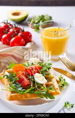 Gaufres belges fraîches avec œufs, tomates, micro-vert et avocat servis sur une assiette avec jus d'orange sur une table en marbre. Petit déjeuner sain Banque D'Images