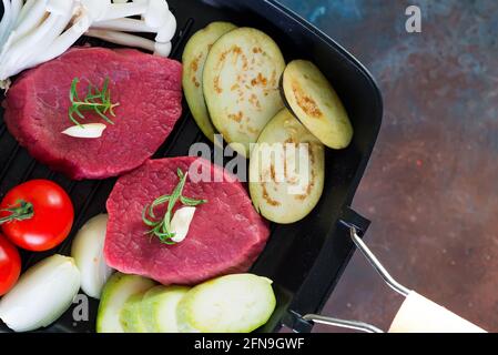 Steaks juteux crus dans une casserole prête à rôtir sur fond de béton rustique. Steaks de viande de bœuf frais aux herbes, à l'ail, au poivre, au sel et aux tomates. Banque D'Images