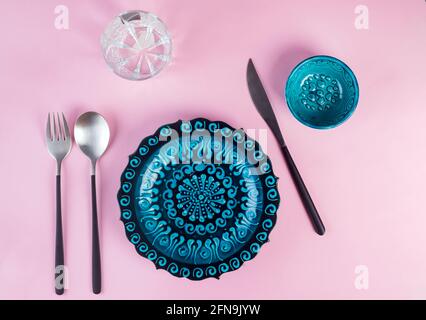 Céramique turque assiette bleue décorée avec de nouveaux couverts noirs de luxe sur fond rose, vue de dessus Banque D'Images