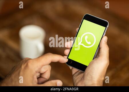 Homme tenant un smartphone dans un café. Logo WhatsApp à l'écran. Mise au point sélective. Banque D'Images