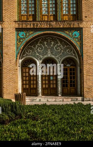 Mur du palais de Golestan avec carreaux de céramique peints et une niche ovale décorée d'un motif de stuc blanc sur trois portes doubles en bois. Banque D'Images