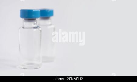 Deux flacons ou flacons de vaccin en verre corona avec bouchon bleu sur fond blanc. Faible profondeur de champ. Copier l'espace Banque D'Images