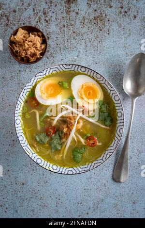 Un seul bol de Soto Ayam (traduction : soupe de poulet indonésienne) avec un œuf dur, un oignon frit et de la coriandre servi avec une cuillère, d'en haut sur un tex Banque D'Images