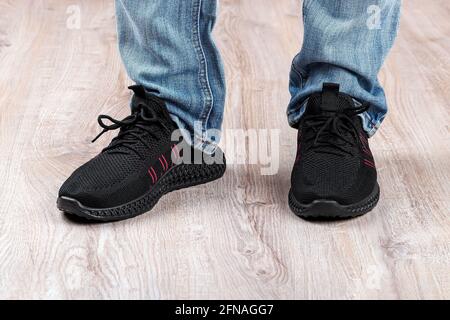 Homme en jeans bleus et baskets noires debout sur un sol brun clair. Pieds debout dans des chaussures décontractées à lacets en mesh pour un style de vie actif et une vie quotidienne Banque D'Images