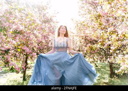 Une fille dans une robe bleue coulant marche à travers un jardin rose fleuri. Banque D'Images