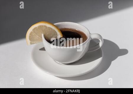 Tasse de café avec espresso servie avec du citron sur fond blanc avec ombres et lumière du soleil Banque D'Images