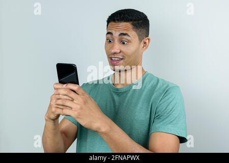 Homme brésilien de 28 ans, tenant le smartphone dans les deux mains et faisant un visage surpris. Banque D'Images