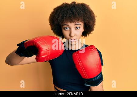 Jeune fille sportive hispanique utilisant des gants de boxe décontracté avec une expression sérieuse sur le visage. Simple et naturel regarder la caméra. Banque D'Images
