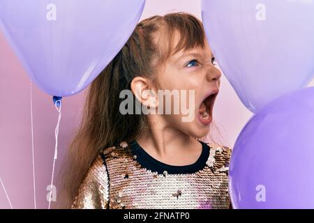 Petite fille caucasienne tenant des ballons en colère et fou hurlant frustré et furieux, criant avec colère. Rage et agressif concept. Banque D'Images