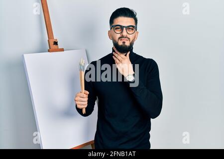 Beau homme avec la barbe tenant des brosses près du chevalet se touchent le cou douloureux, mal de gorge pour la grippe, la motte et l'infection Banque D'Images
