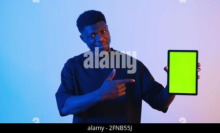 Homme noir afro-américain tenant une tablette numérique avec un écran vert pointant vers la tablette. Photo de haute qualité Banque D'Images
