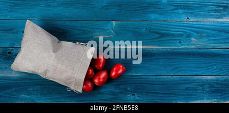 Le sac de toile de jute fera déborder les tomates sur bleu rustique table en bois Banque D'Images