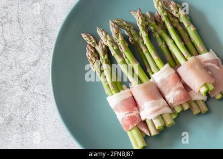 Asperges enrobées de bacon sur une assiette verte bleue. Avec un arrière-plan concret Banque D'Images