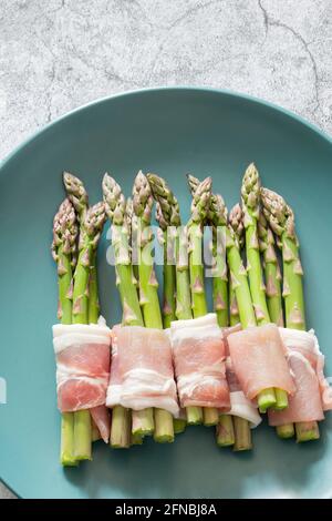 Asperges enrobées de bacon sur une assiette verte bleue. Avec un arrière-plan concret Banque D'Images