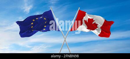 Drapeaux de l'Union européenne et du canada agitant dans le vent sur des mâts de drapeaux contre le ciel avec des nuages le jour ensoleillé. Symbolisant la relation, le dialogue entre deux Banque D'Images