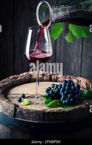 Verser le vin rouge de la carafe dans un verre et des raisins foncés. Industrie du vin. Banque D'Images