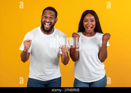 Portrait d'un heureux couple noir célébrant la victoire avec des poings levés Banque D'Images