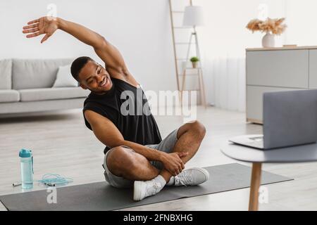 Un homme afro-américain fait de l'exercice d'étirement sur un ordinateur portable à la maison Banque D'Images