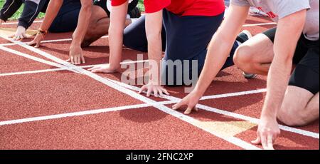 Les garçons du secondaire suivent des courses et des coureurs sur le terrain à la ligne de départ, prêts à démarrer une course de sprint sur une piste rouge sur piste et sur le terrain. Banque D'Images